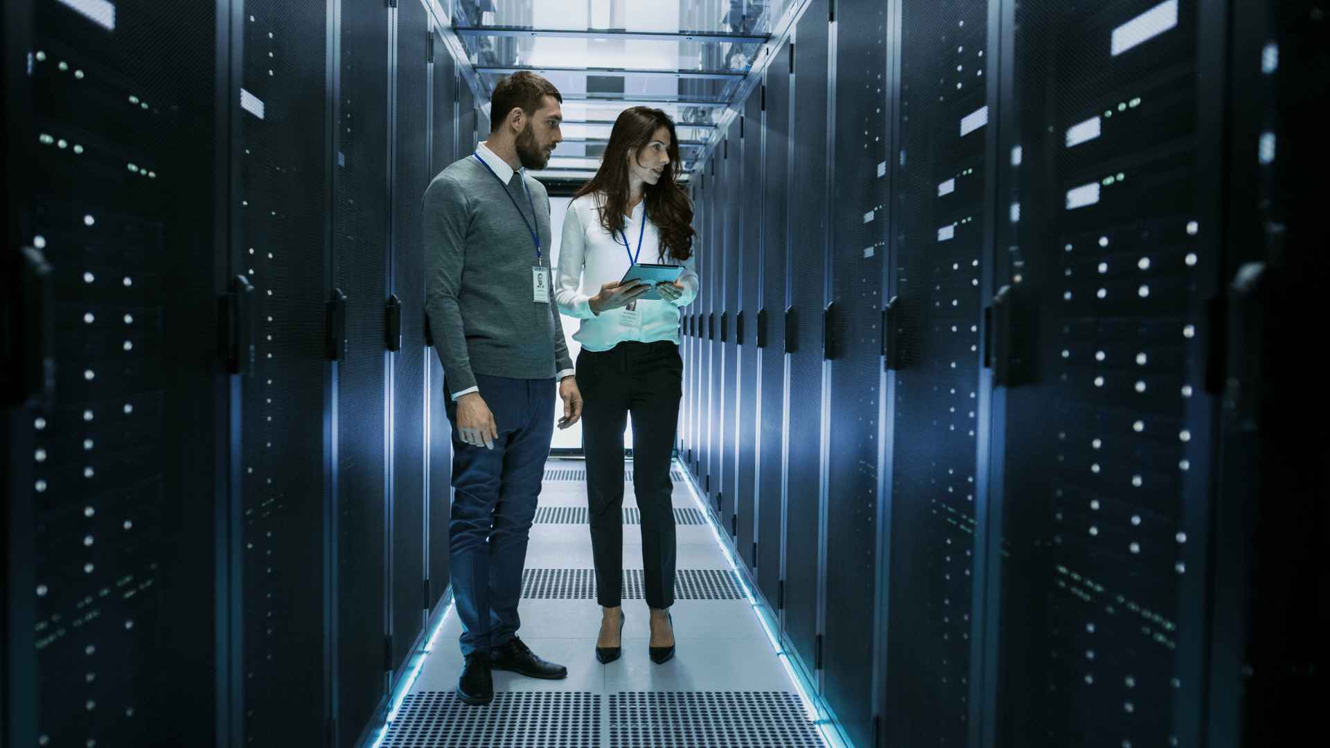 Two individuals standing in a server room, surrounded by rows of servers and networking equipment.