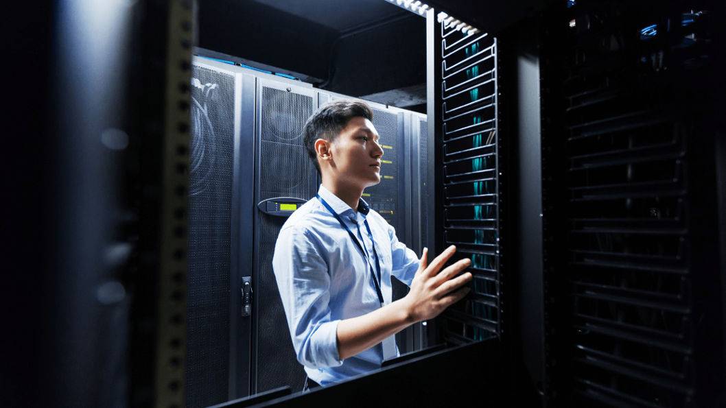 A man in a shirt and tie examines a server, showcasing a professional tech environment.