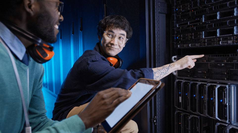 Two men examining a tablet while standing in front of a server rack, engaged in a technical discussion.