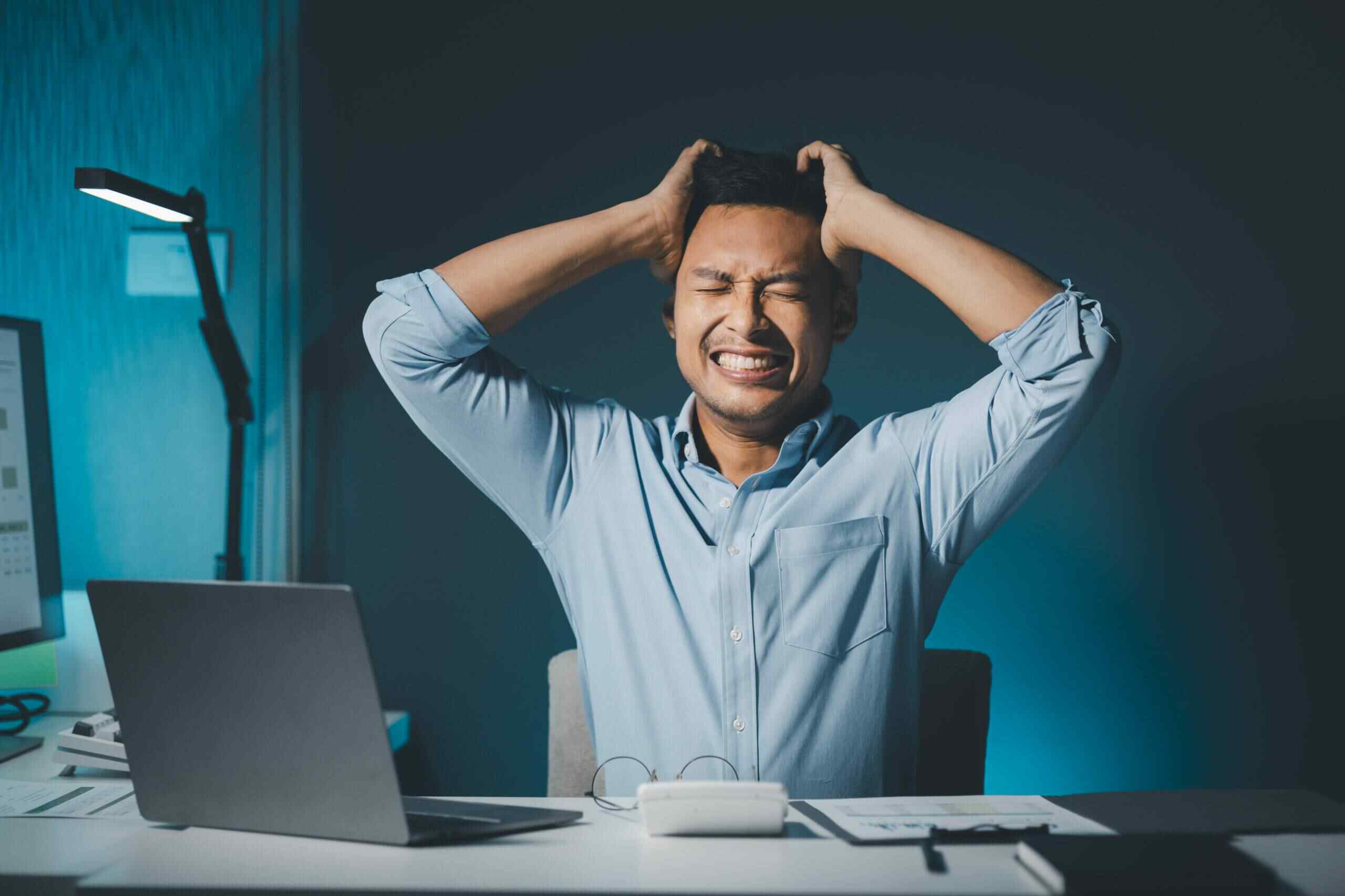 A man at his desk, visibly stressed, with his head resting in his hands, reflecting a moment of frustration or overwhelm.