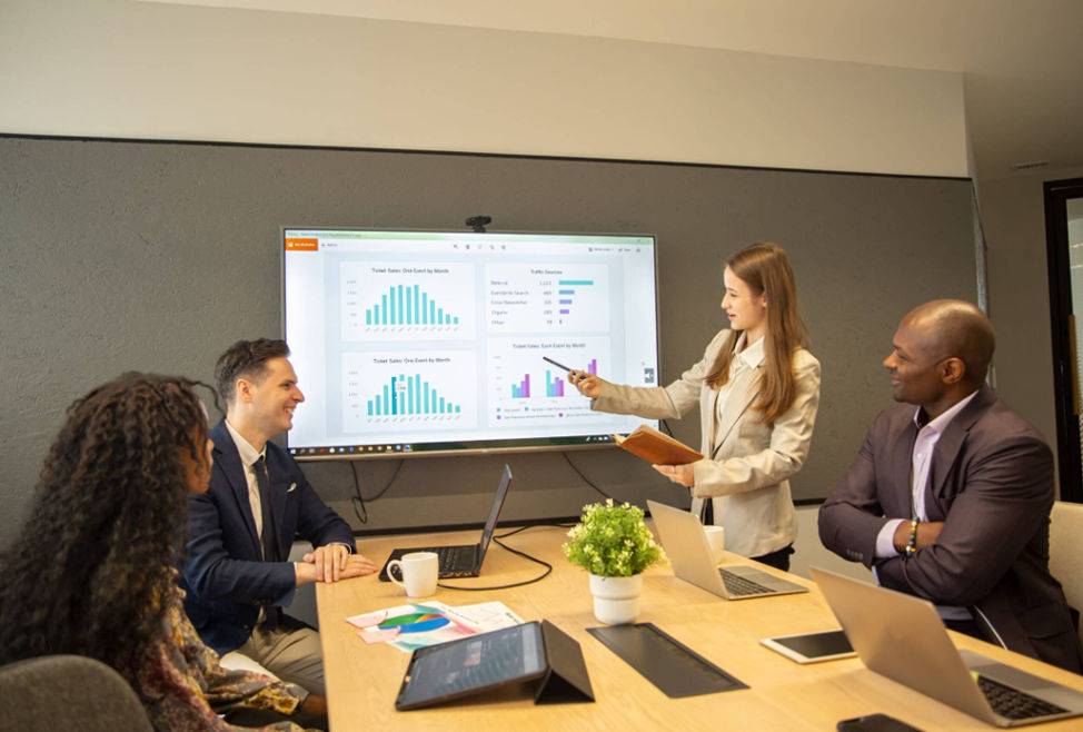 A diverse group of professionals engaged in discussion around a large screen in a modern meeting room.