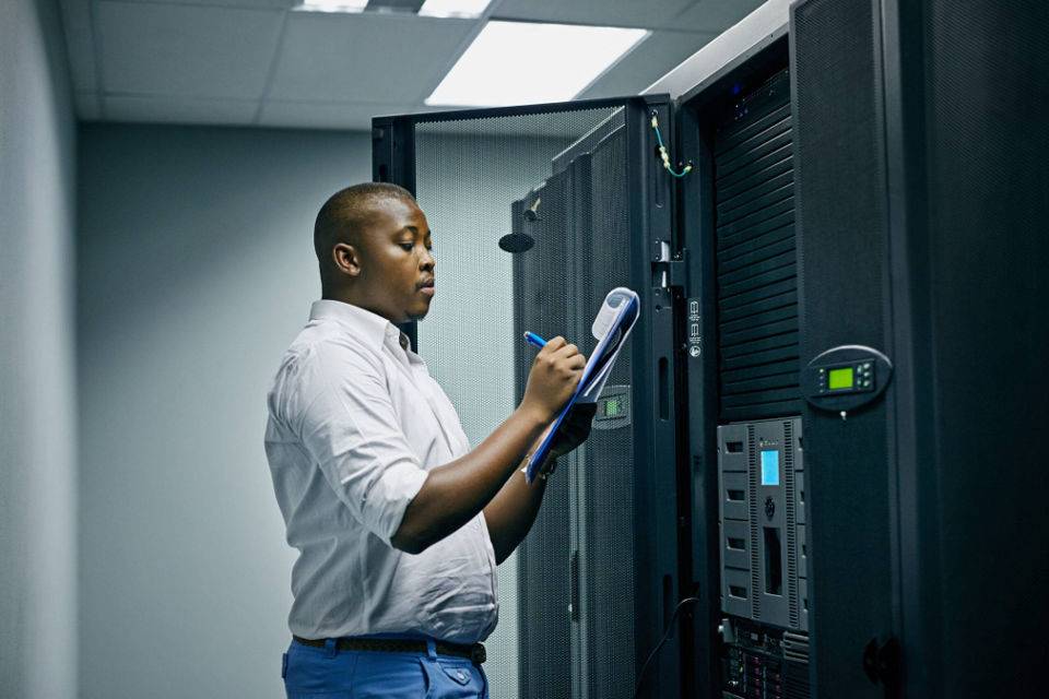 A man stands confidently in front of a server rack, showcasing a modern data center environment.