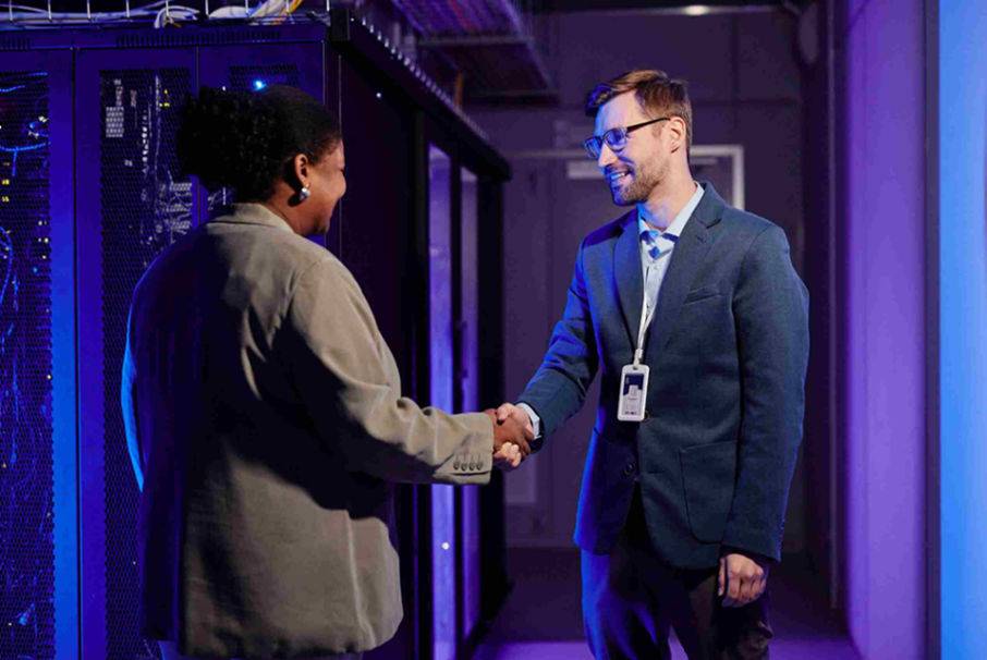 Two individuals shaking hands in front of a server rack, symbolizing partnership and collaboration in technology.