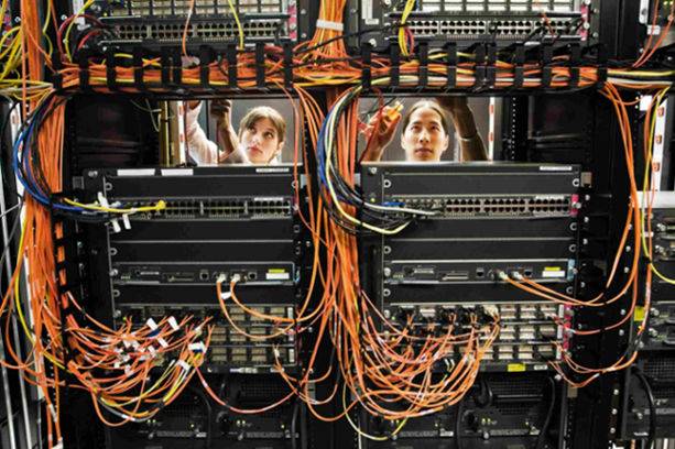 Two women are cabling servers while standing in a server room filled with computer equipment and servers.