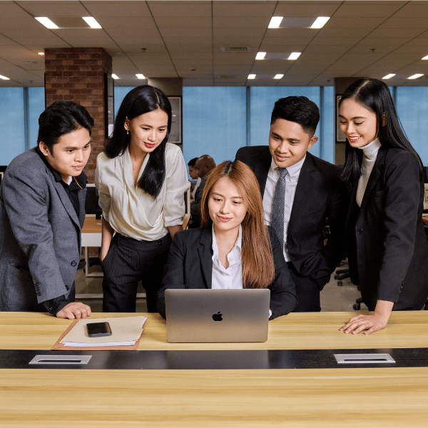 Employees from TRT Total RISC Technology collaborating around a table, focused on a laptop in a professional office setting