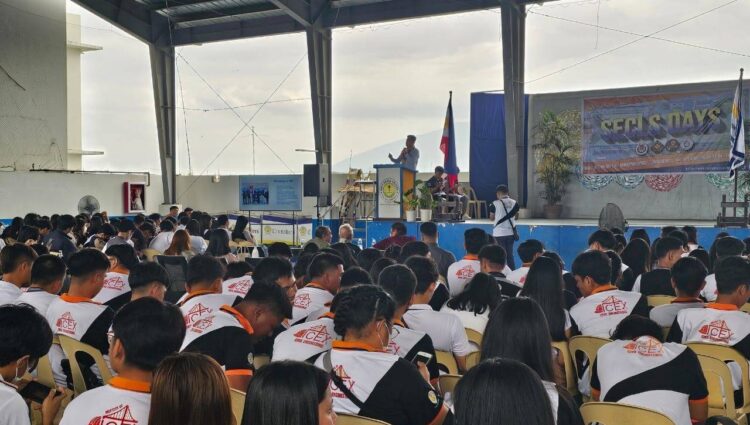 A diverse group of people in chairs, attentively watching a stage presentation at Holy Cross College's TRT Corporate Social Responsibility event.